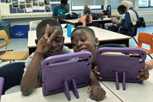 Two kids smiling while on IPads with purples cases.