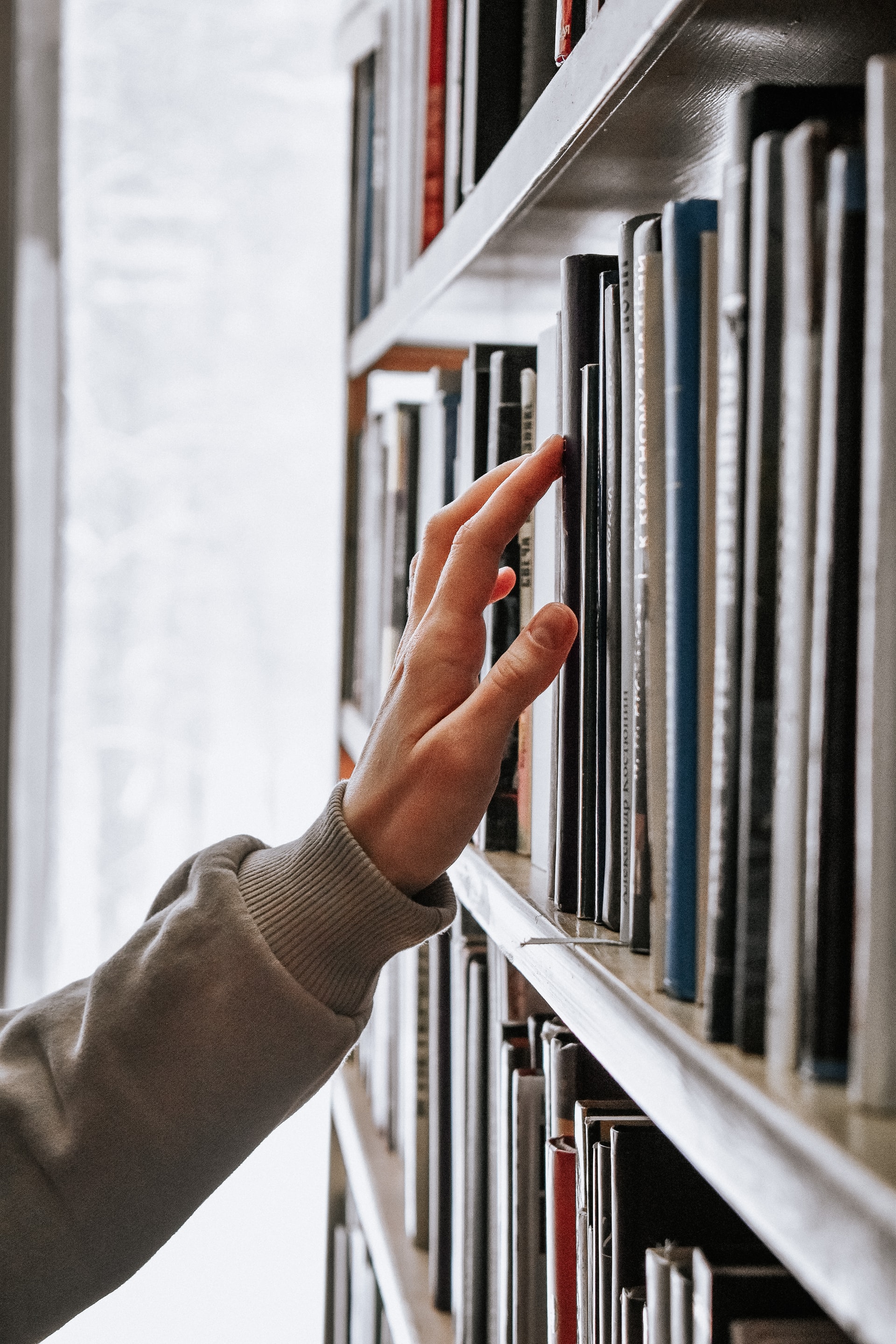 a hand on a book crest, library shelves