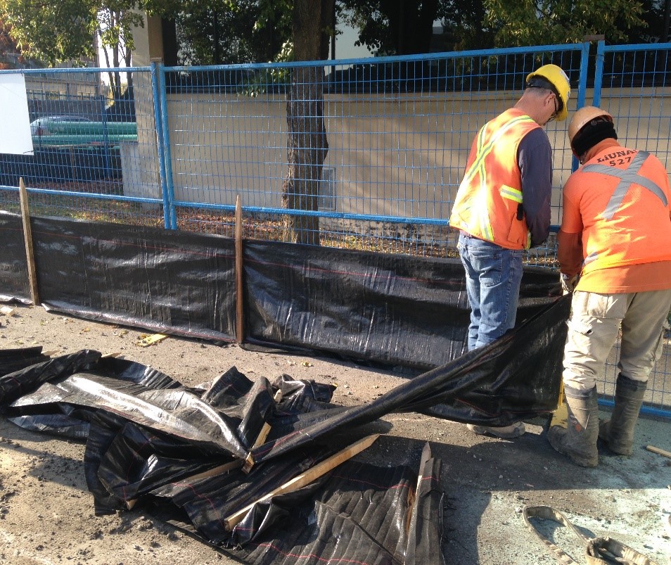 Contractors setting up a silt fence to ensure sediment control at a worksite.