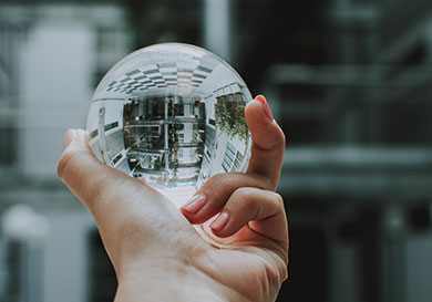 A person holding a clear crystal glass ball with the reflection of a building