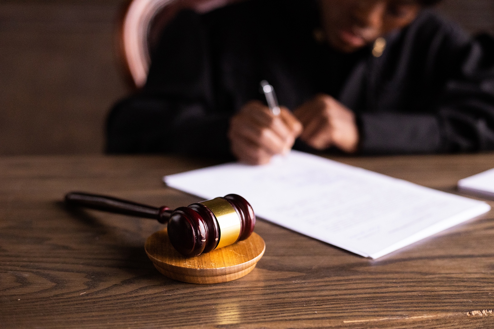 A judge sitting at a desk writing on a piece of paper. A gavel lies on the table.