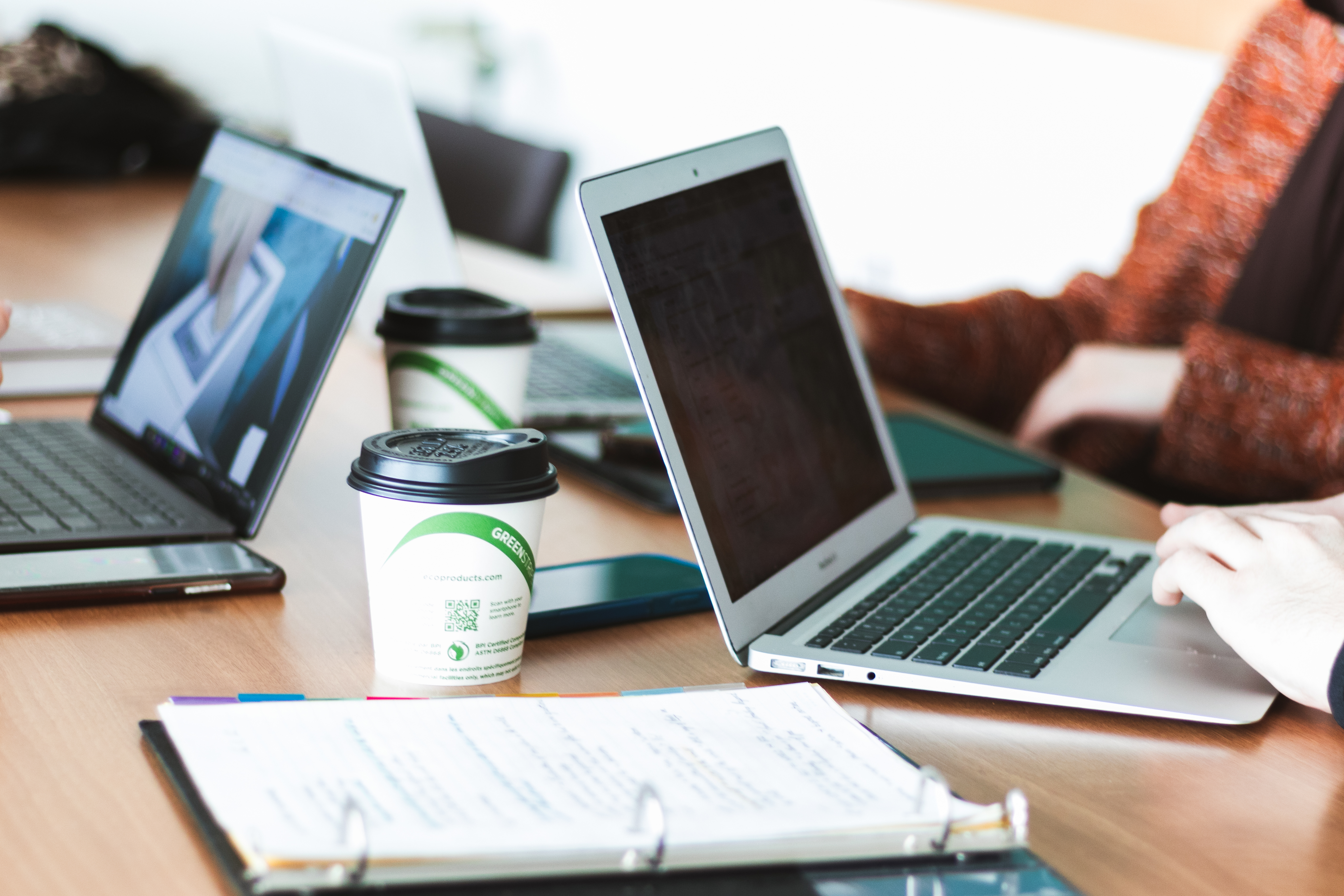 People working on laptops around a meeting table with coffee cups and notes in the foreground.