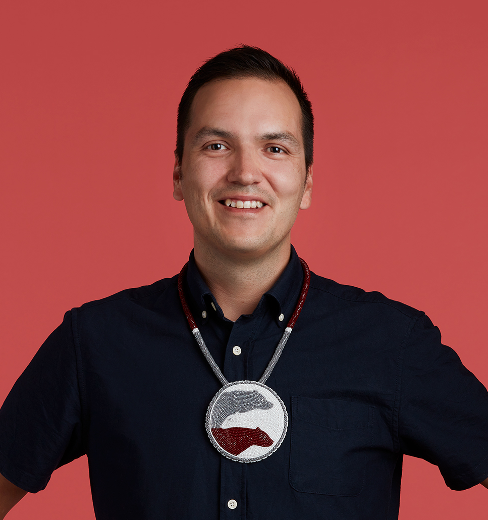 Image shows Darren Sutherland, a Cree man, wearing a blue collared shirt with a beaded medallion depicting three bears on his chest.