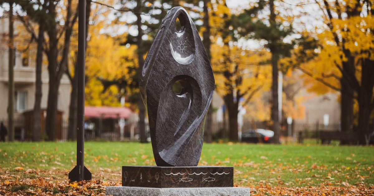 Image shows a statue, described as the abstract form of a woman wrapped in a shawl, with trees in the background.
