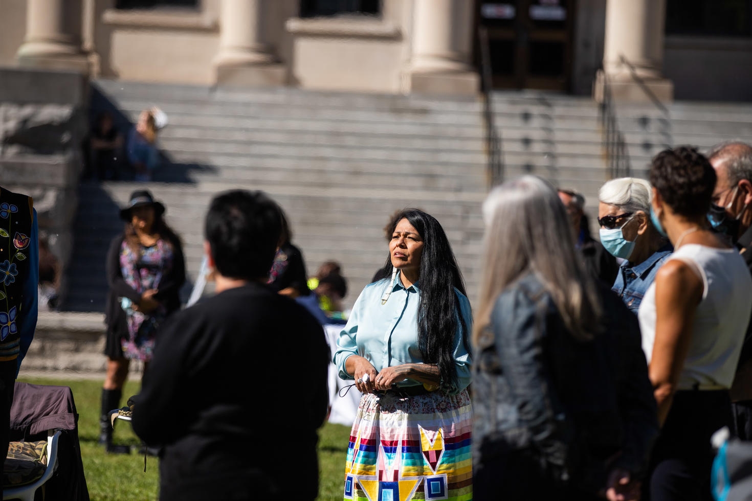 Group of indivduals. Most are blurred but one woman appears prominently in the center. She appears to be speaking to the group around her.