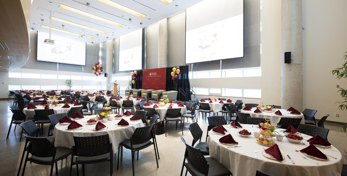 Event room setup with round tables, chairs, a stage and screens for networking meal.