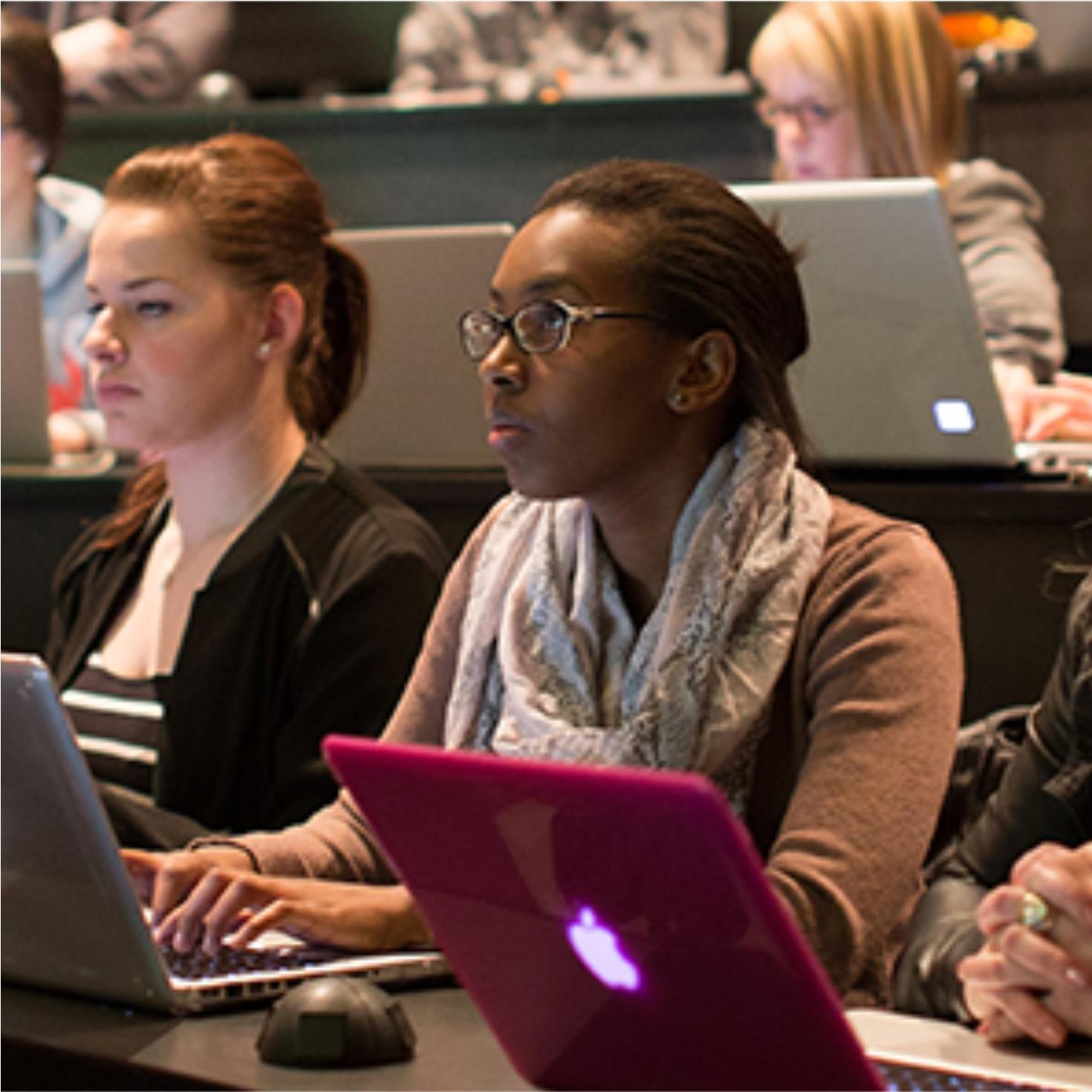 Students in class typing on laptops listening to lecture.