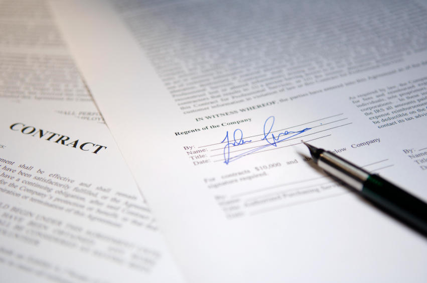 Paper contracts spread out over desk with pen.