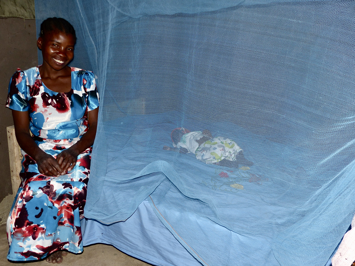 African woman sitting on bed where child sleeps inside said net
