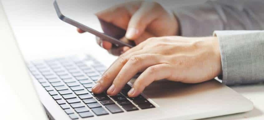 A person using a laptop and their cellphone together