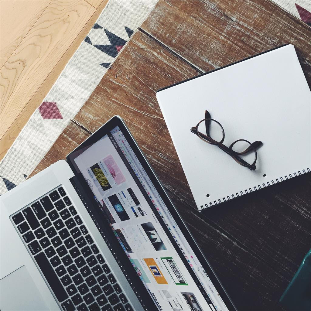  Laptop on wooden table with reading glasses and papers