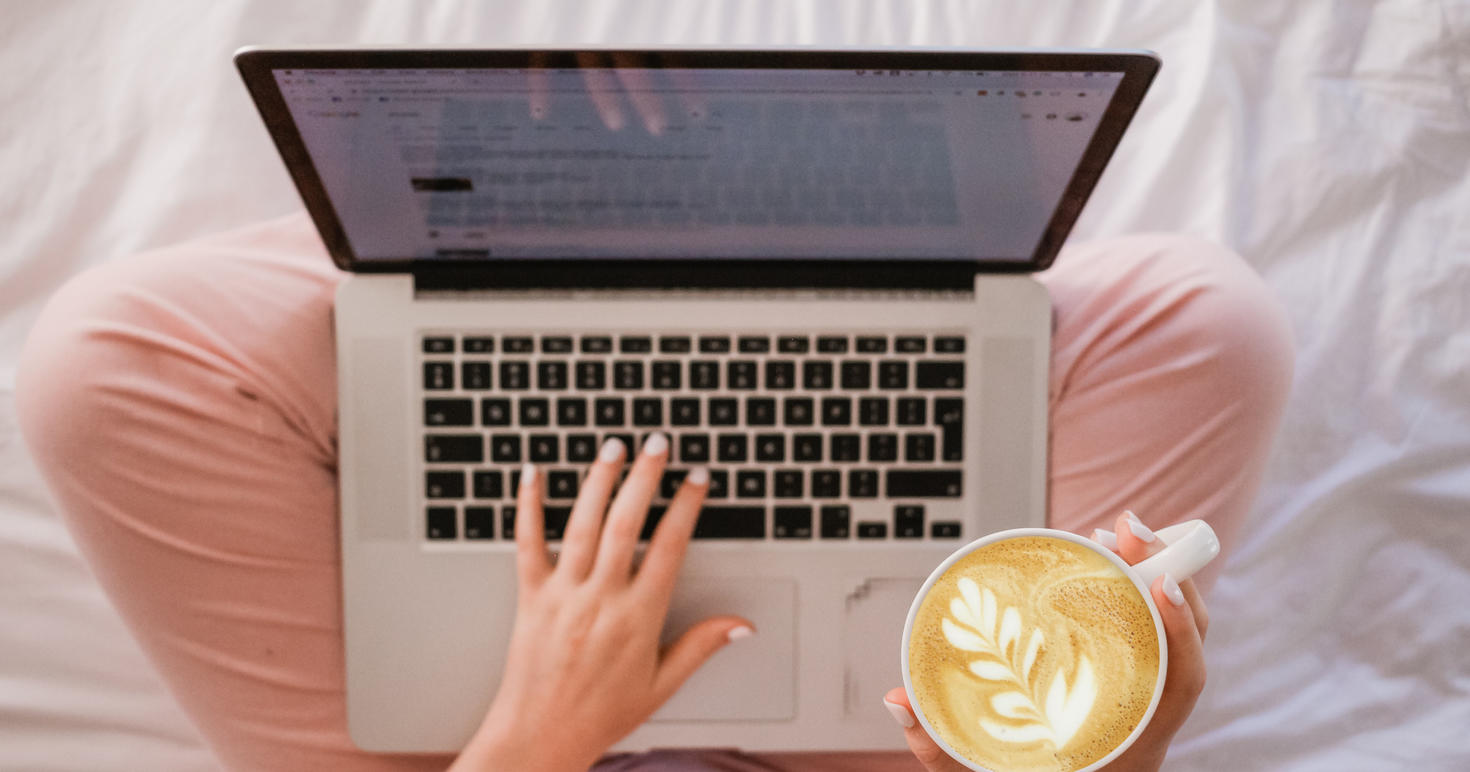 A person on a laptop holding a latte