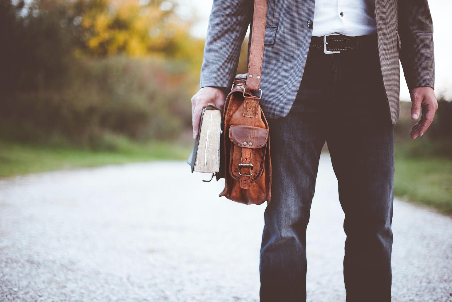 A man with his handbag and a book in his hand.