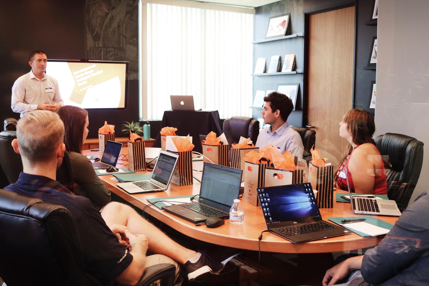 Colleagues sitting at a board meeting with laptops and gift bags.
