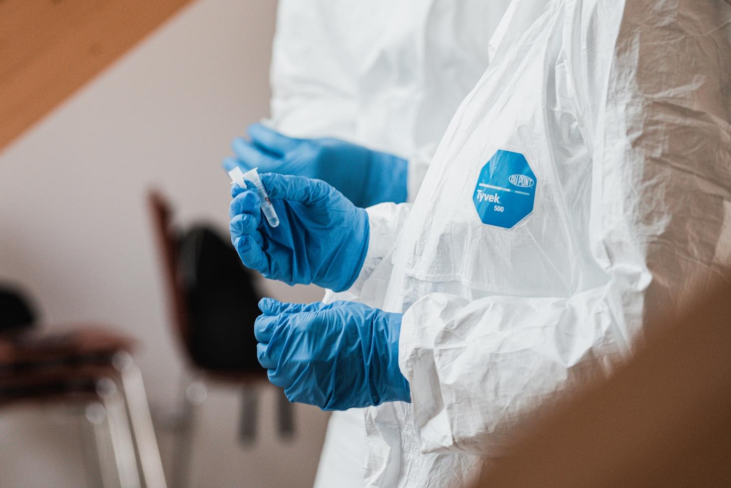 PPE covered person holding PCR COVID tube