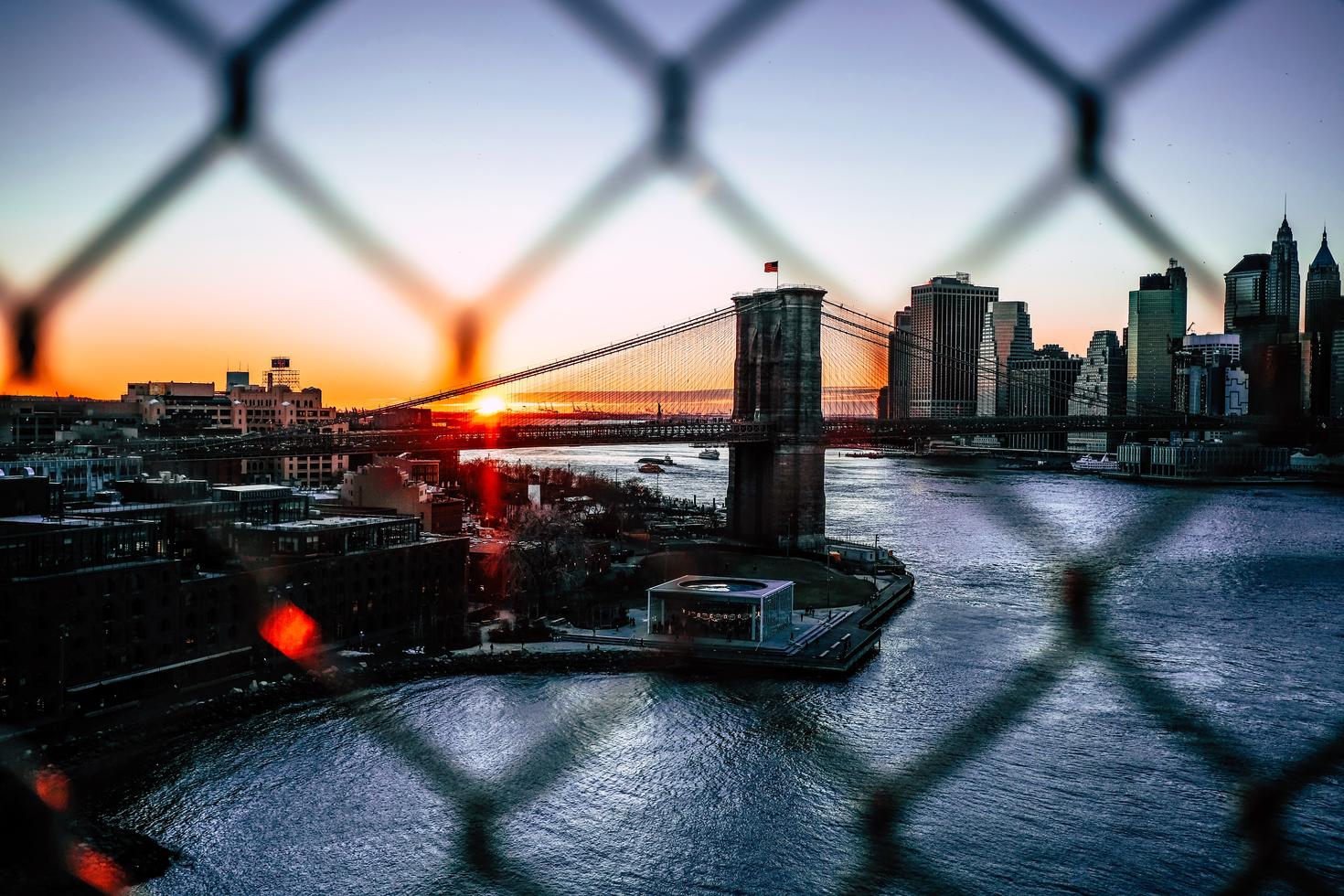 Photo of a gate and a sunset on a city in background.