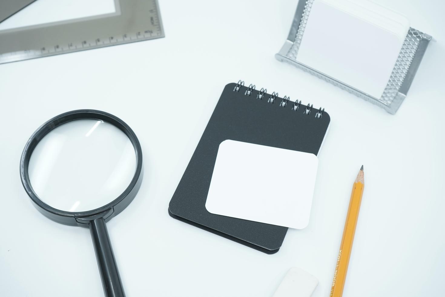 A magnifying glass at the side of a ruler, note book and a pensil.