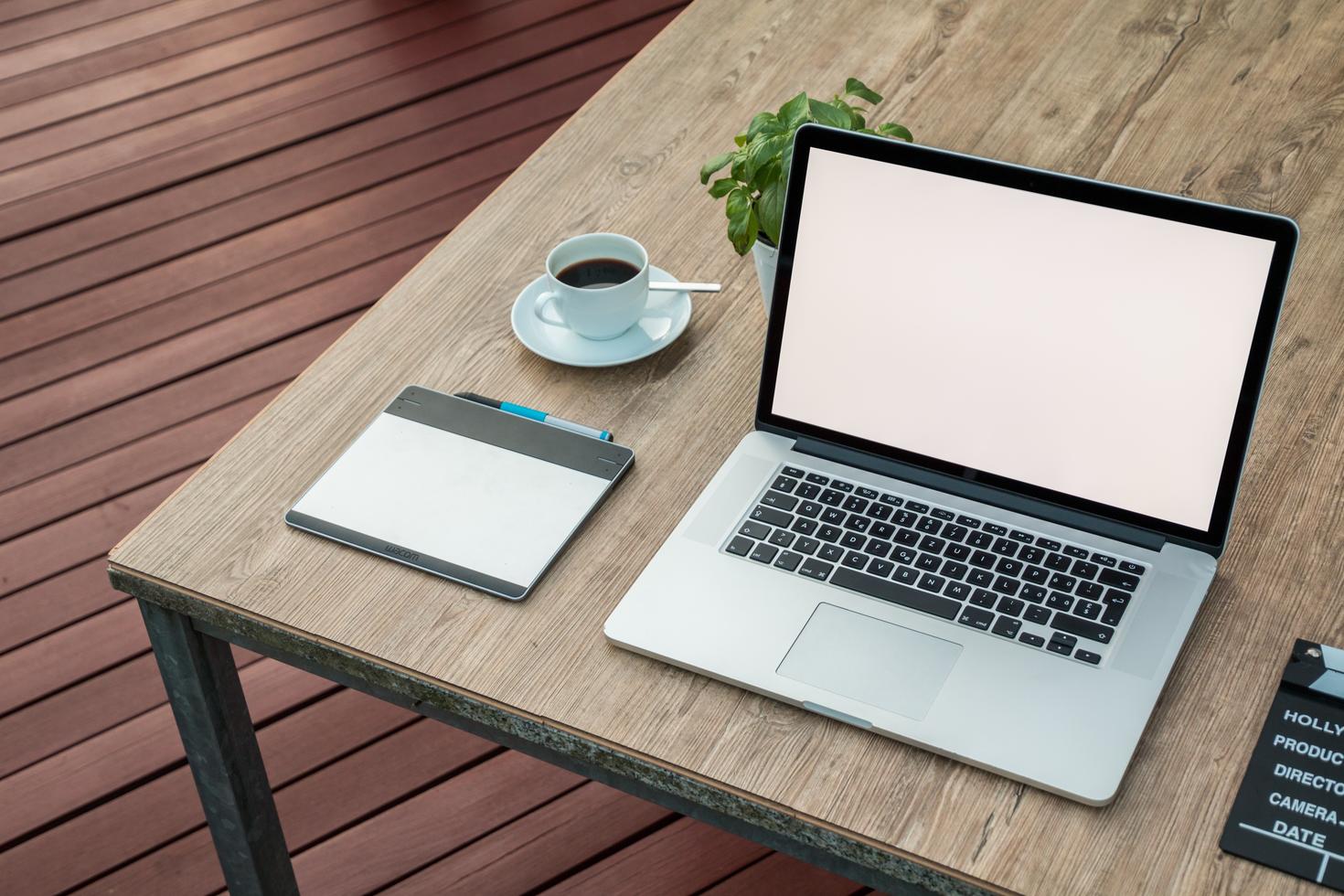 Wooden table with coffee cup, plant, tablet, movie clapboard and laptop on it.