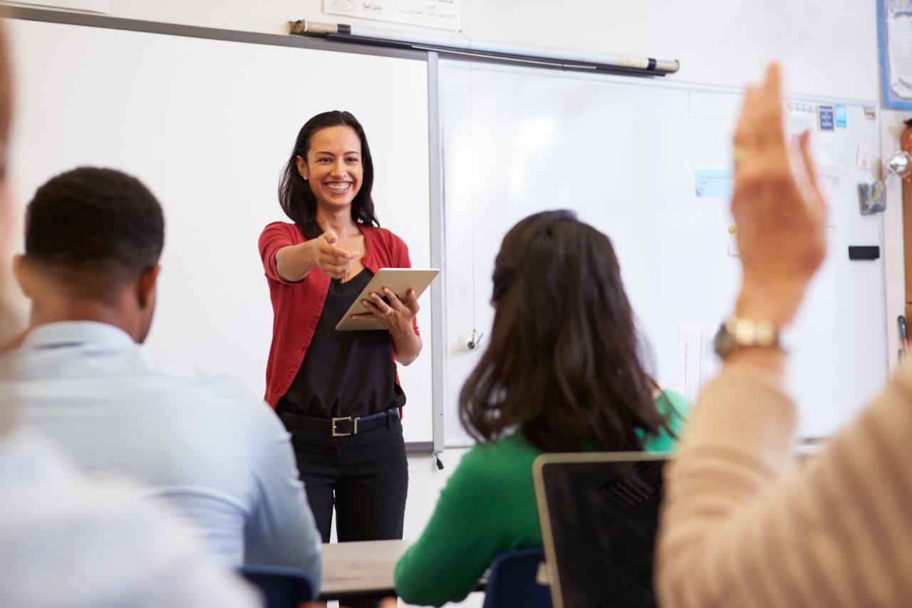 A smiling women teacher in a classroom with university students.