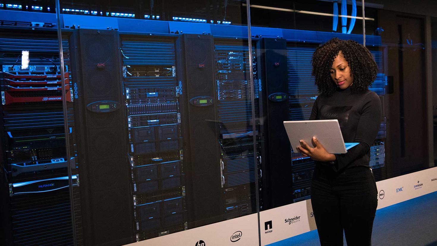 Women with a computer standing in a server room performing maintenance tasks.