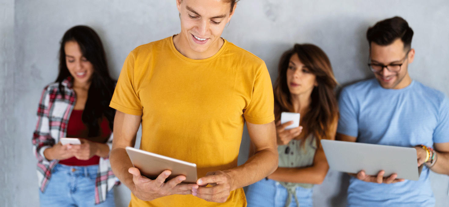 4 students standing in front of a wall holding different devices (smartphone, tablet, laptop)
