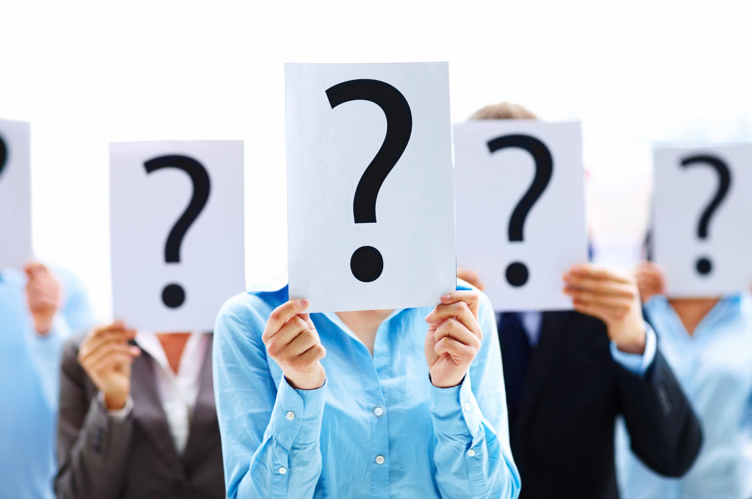 Several people cover their faces with a sheet of paper with a question mark drawn on it.