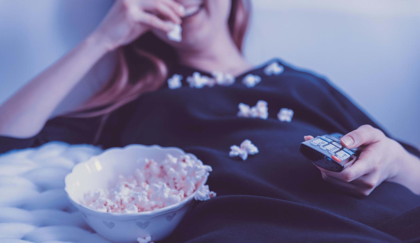 woman lying in bed while eating popcorn