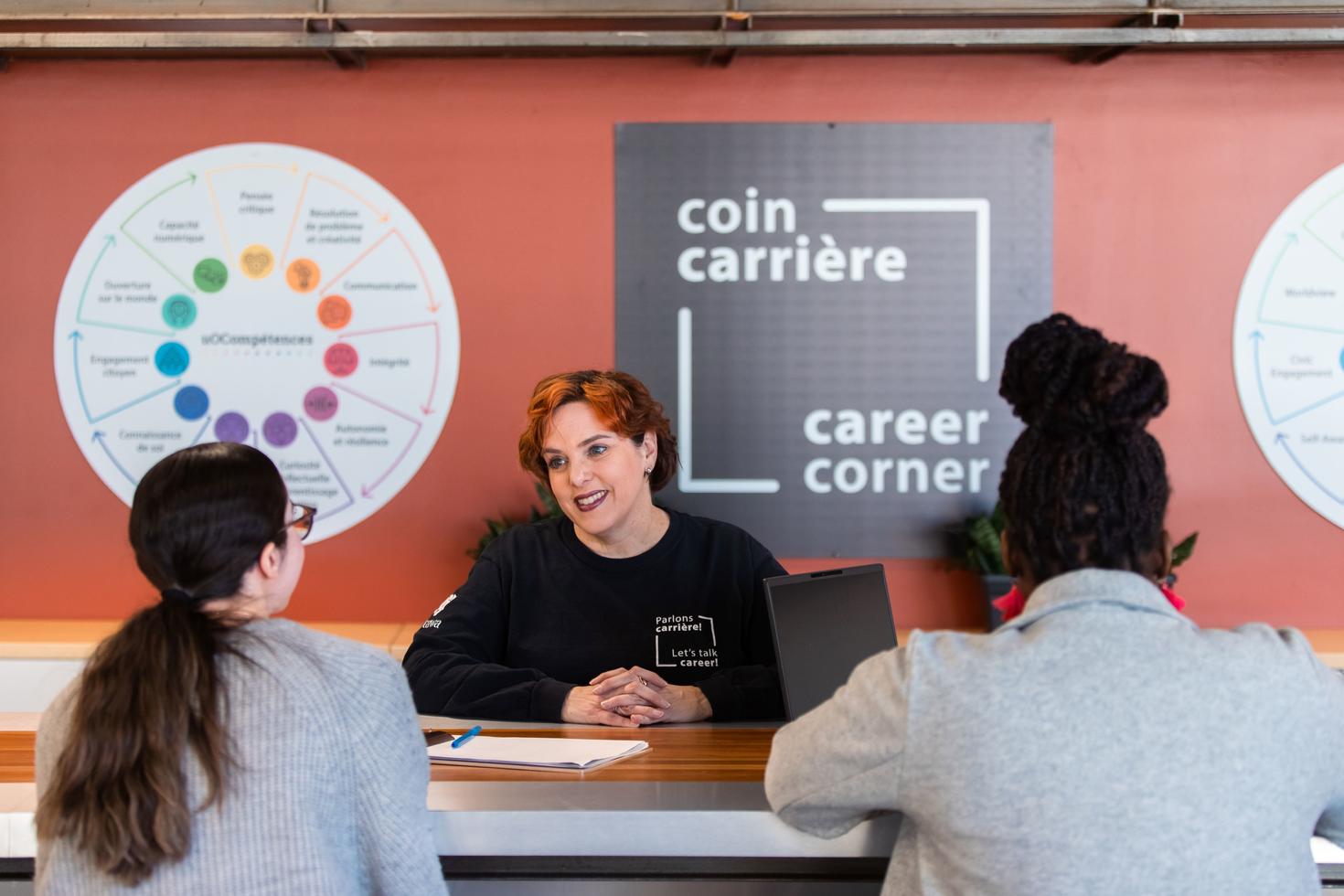 A woman sitting at a table across from two women. There is a poster on the wall with the following text: "Coin carrière, career corner."