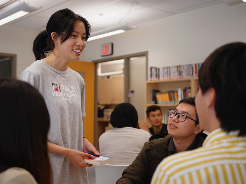 A teacher's assistant talking to a group of students in a library