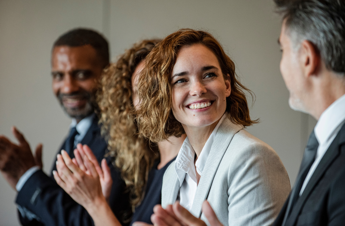 4 individuals in business attire clapping with one looking at the camera