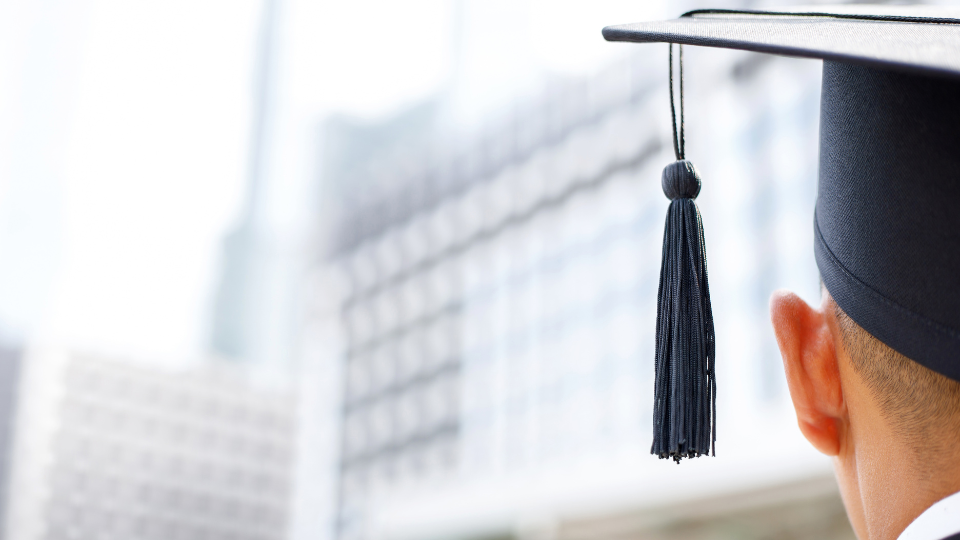 Back of head wearing a graduation hat facing a blurred building