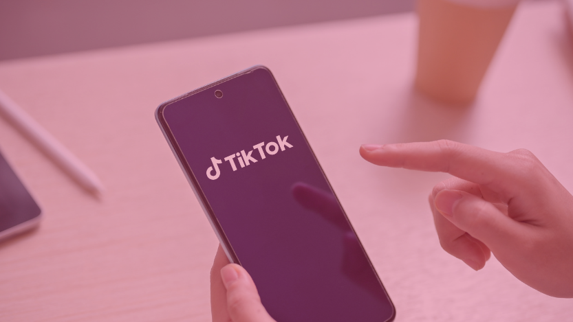 A hand holds a dark smartphone displaying the "TikTok" logo