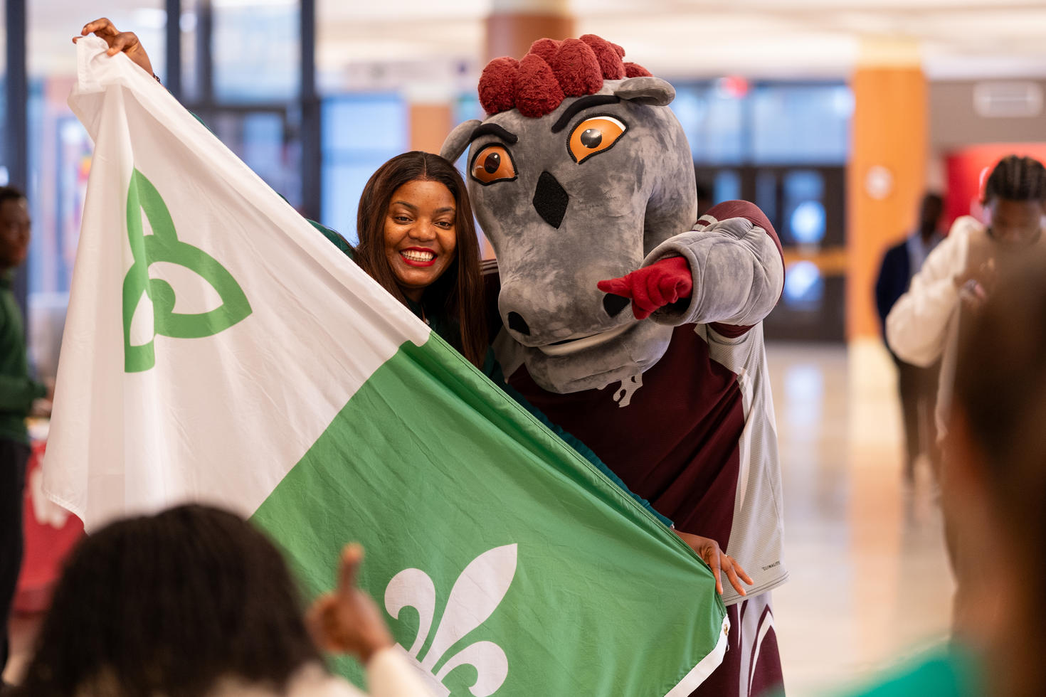 student posing with the GeeGees mascott and the franco-ontarien flag