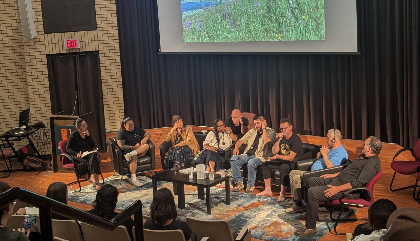 Indigenous people sitting on a stage in front of a room