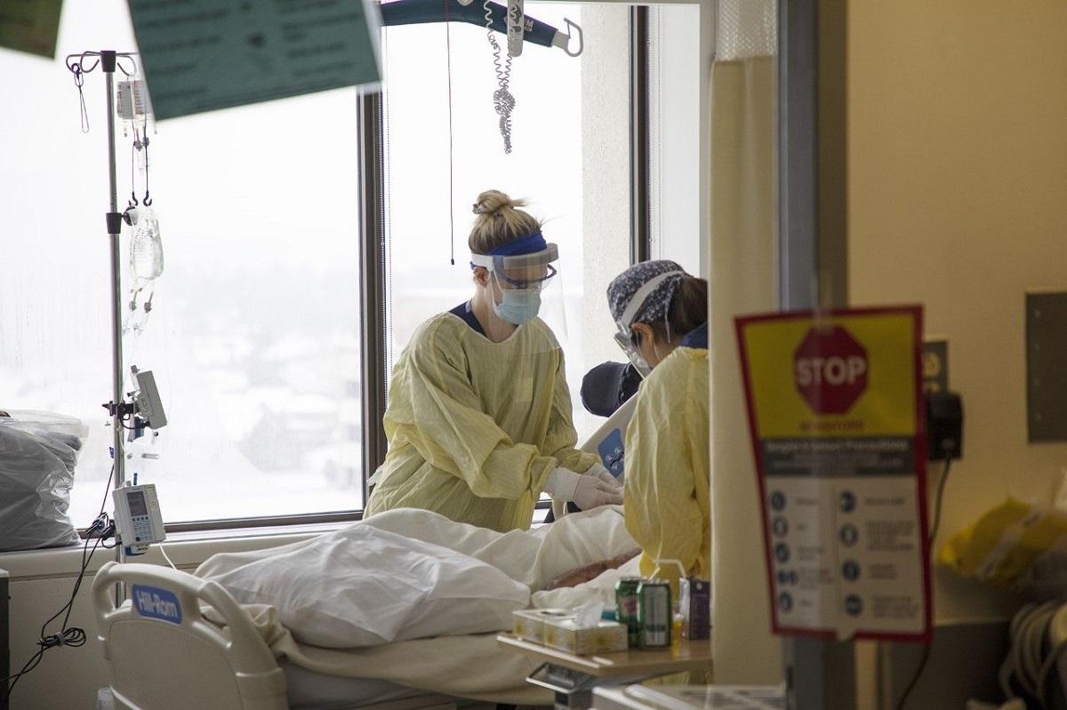 Two healthcare workers in PPE at patient's bedside in hospital