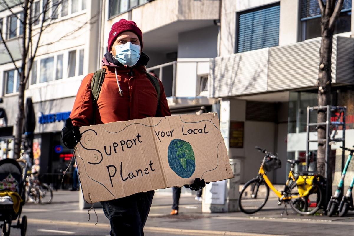 Protestor holding sign reading 'Support your local planet' with drawing of globe on it