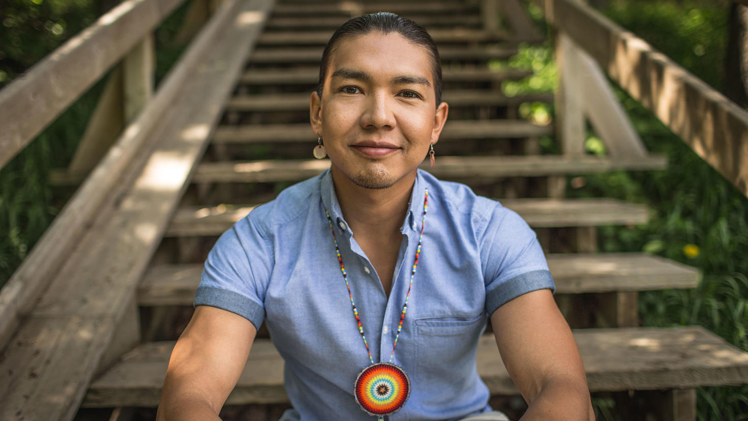 Portrait of James Makokis sitting on wooden steps outside