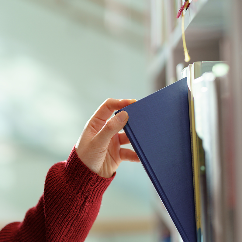 Main d'une personne prenant un livre sur une étagère.