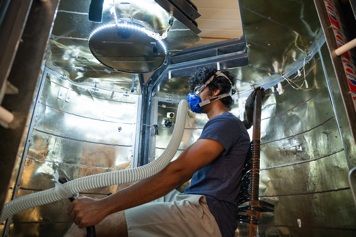 A student sits in a test chamber with an oxygen mask