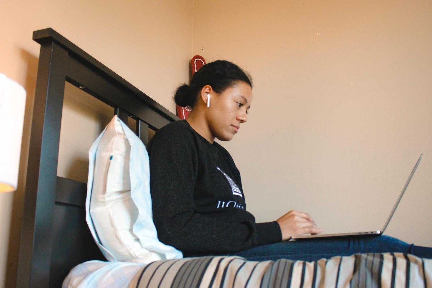 Person sitting on a bed at a computer.