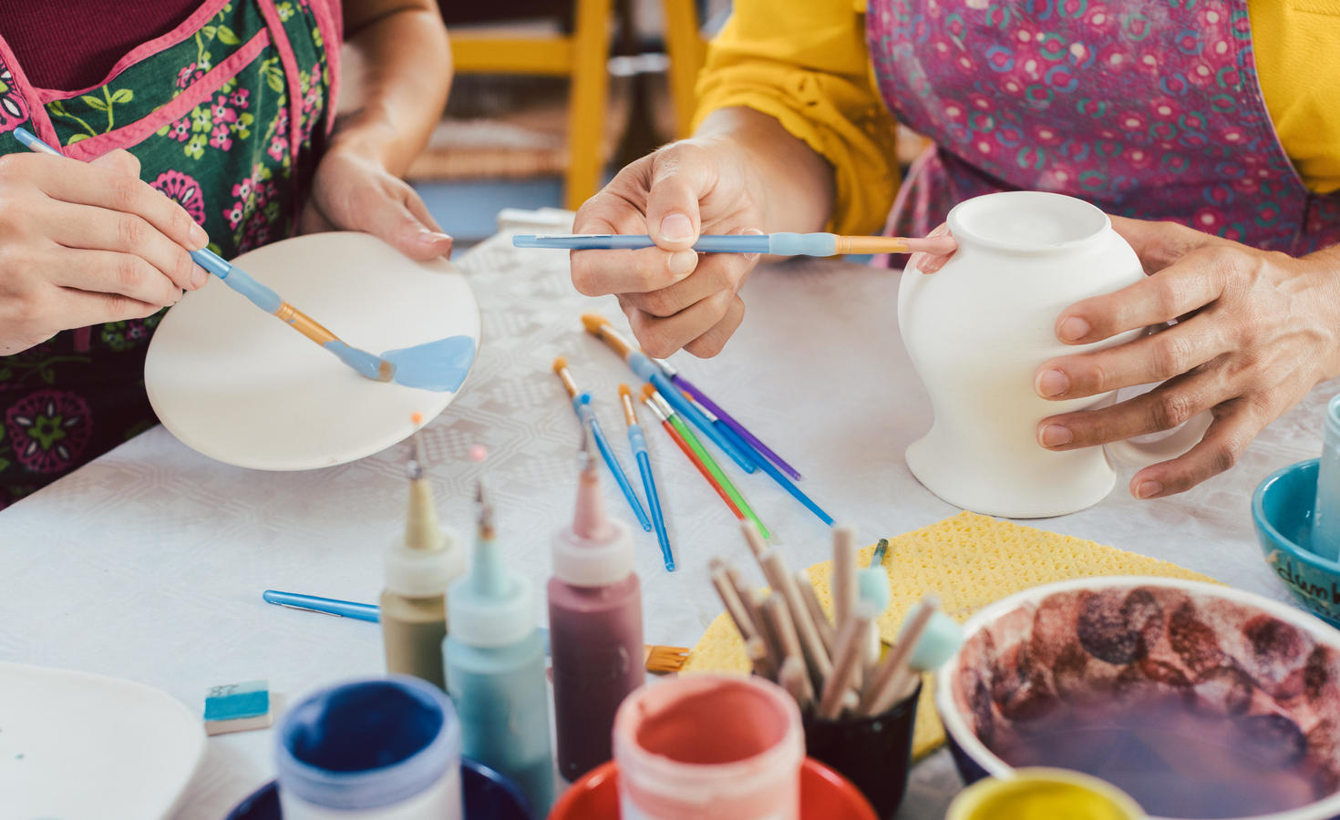 close up of people painting ceramic mugs and plates