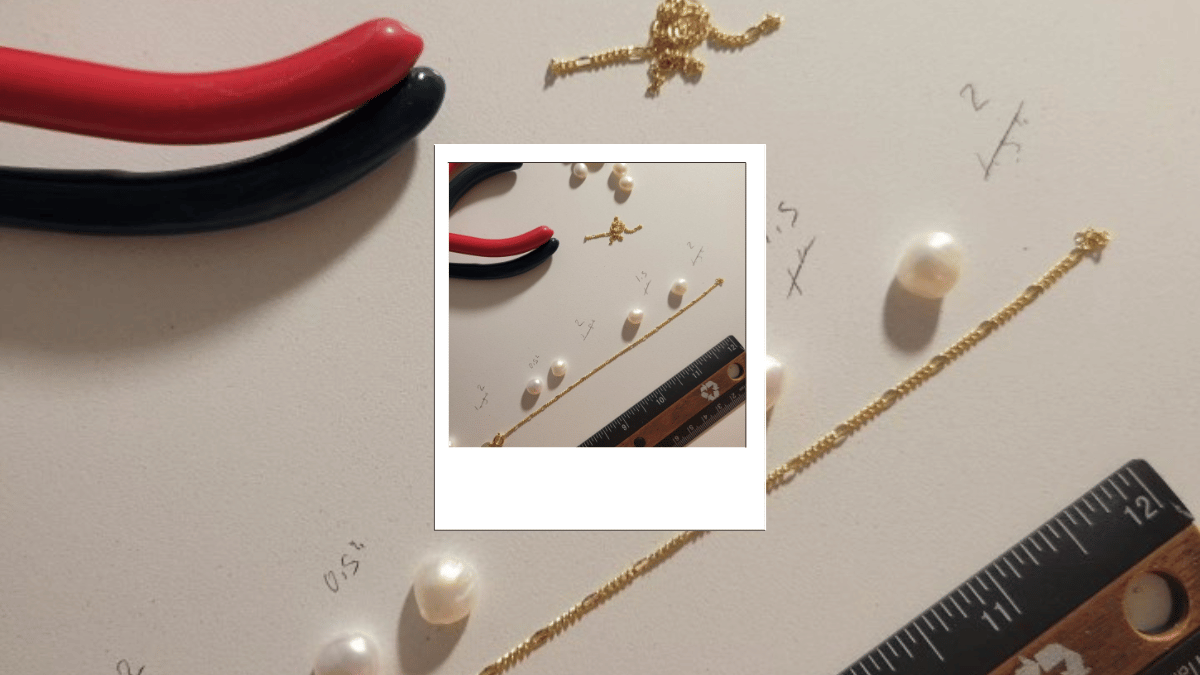 Pearl beads, ruler and gold chain on a white desk top.