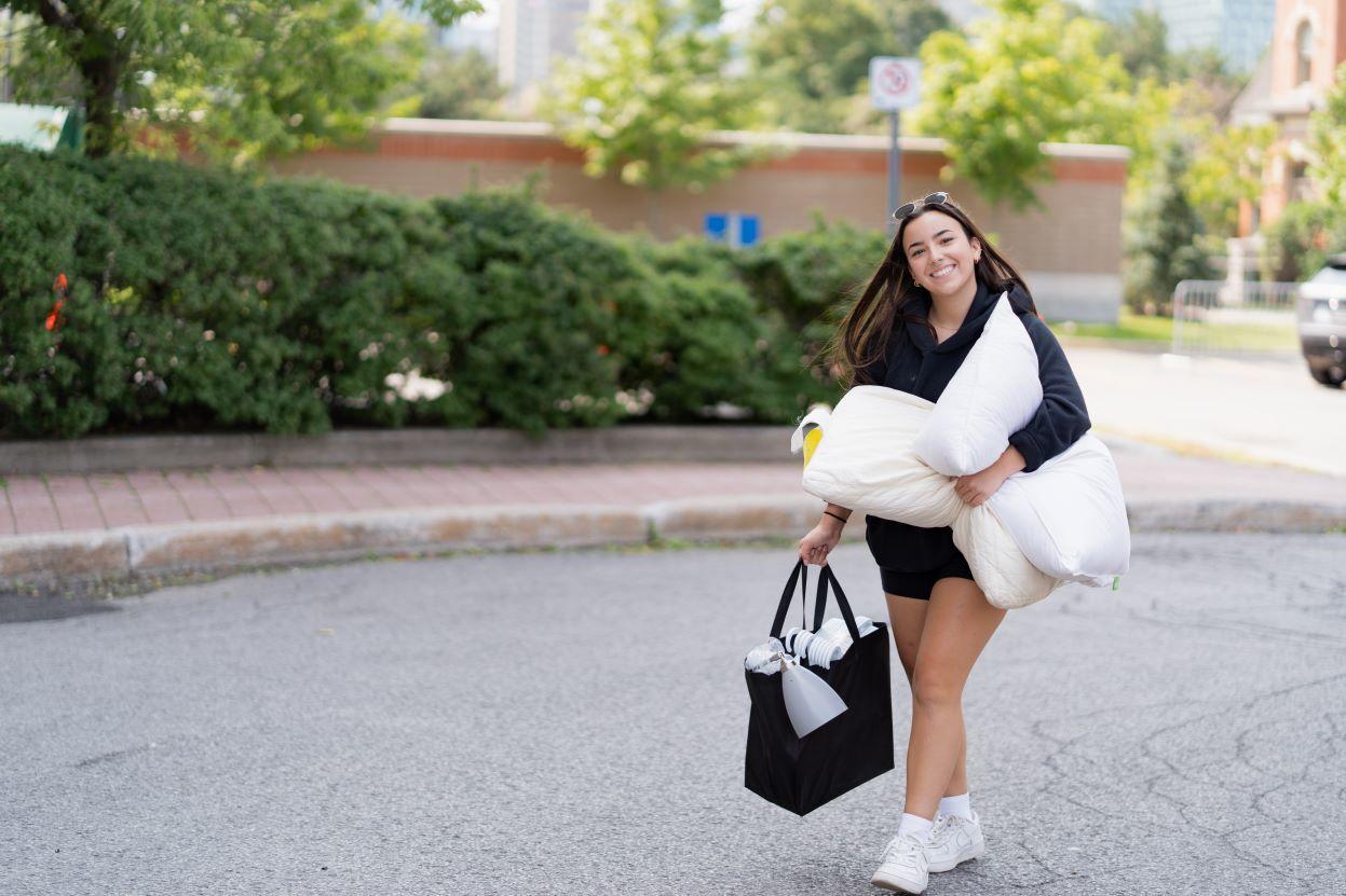 A student carrying two pillows and a bag as she moves in to residence.