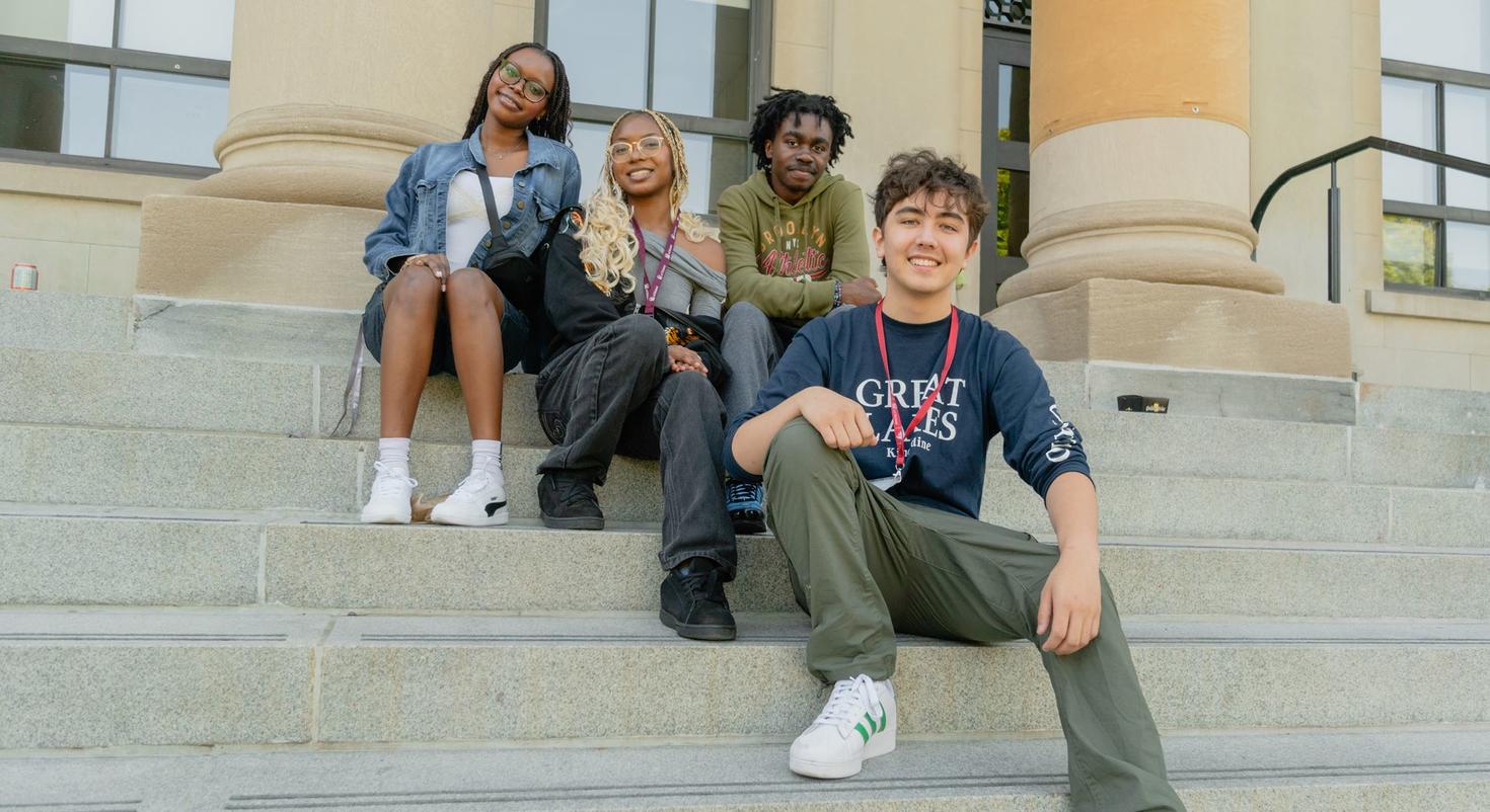 Four international students sit on the steps of the Tabaret building.