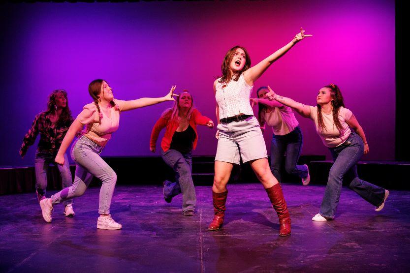 Students sing and dance expressively on stage.