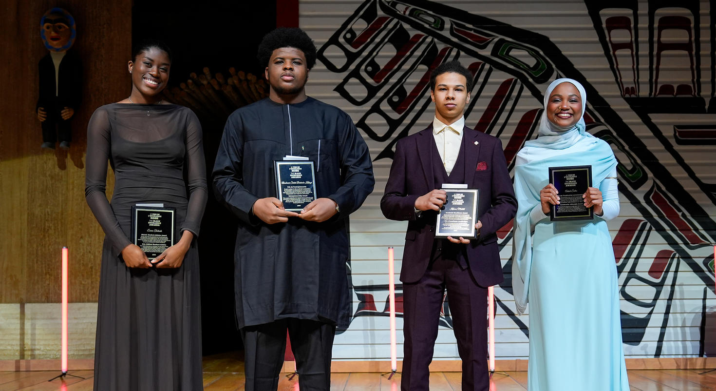 Four winners of the 2026 Black Excellence Awards stand side-by-side on stage, proudly holding their award plaques.
