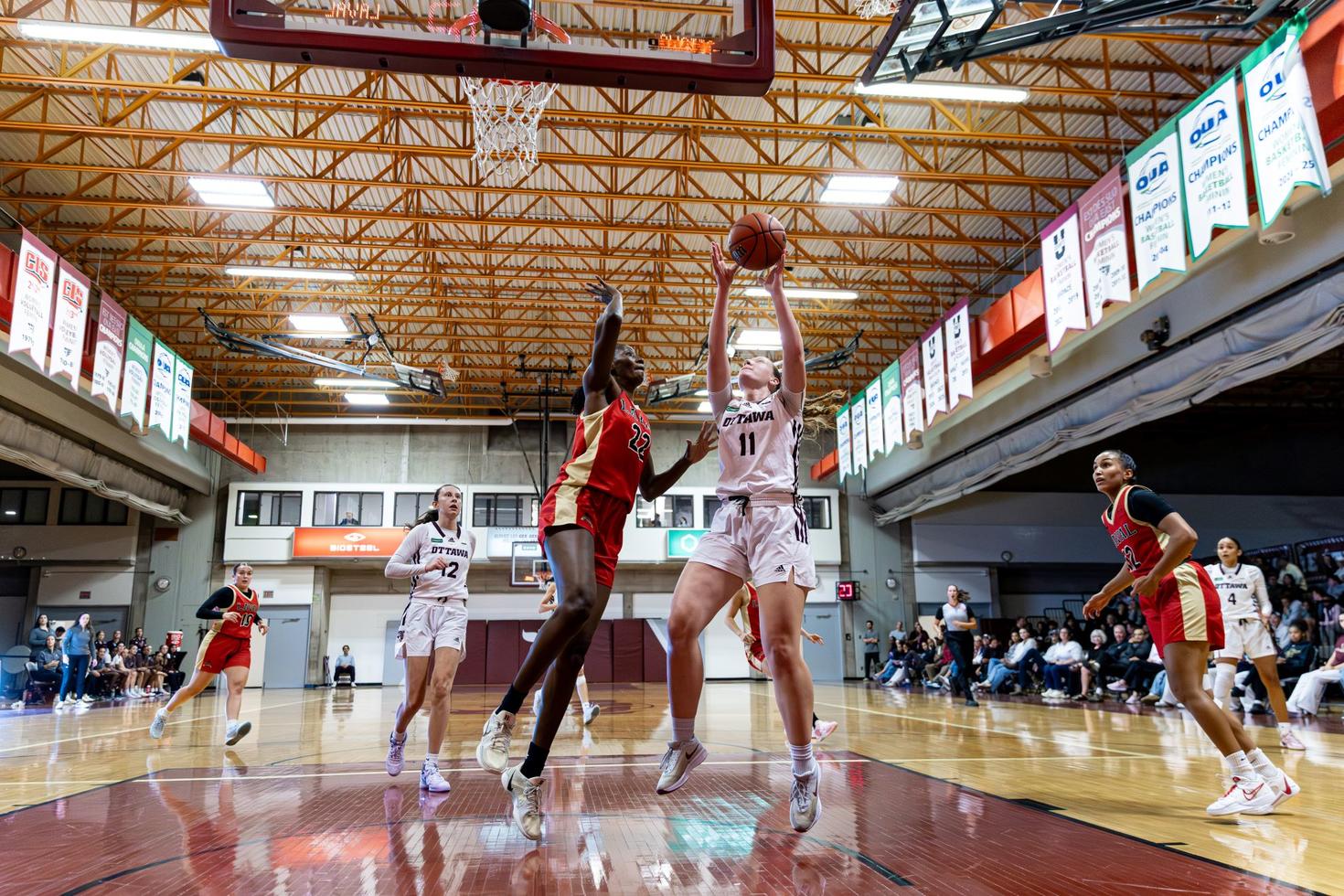 A women's Gee-Gees basketball team player lays up for a shot on the basket as an opposing player attempts to block it.