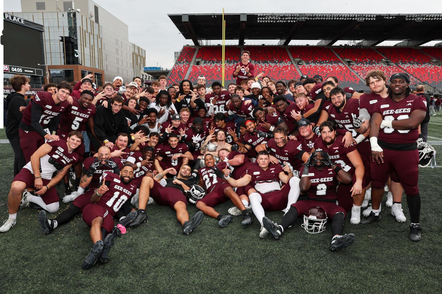 The Gee-Gees men’s football team sprawled out on the field at TD Place holding Pedro the Panda following their October 4, 2026 victory against the Carleton Ravens.