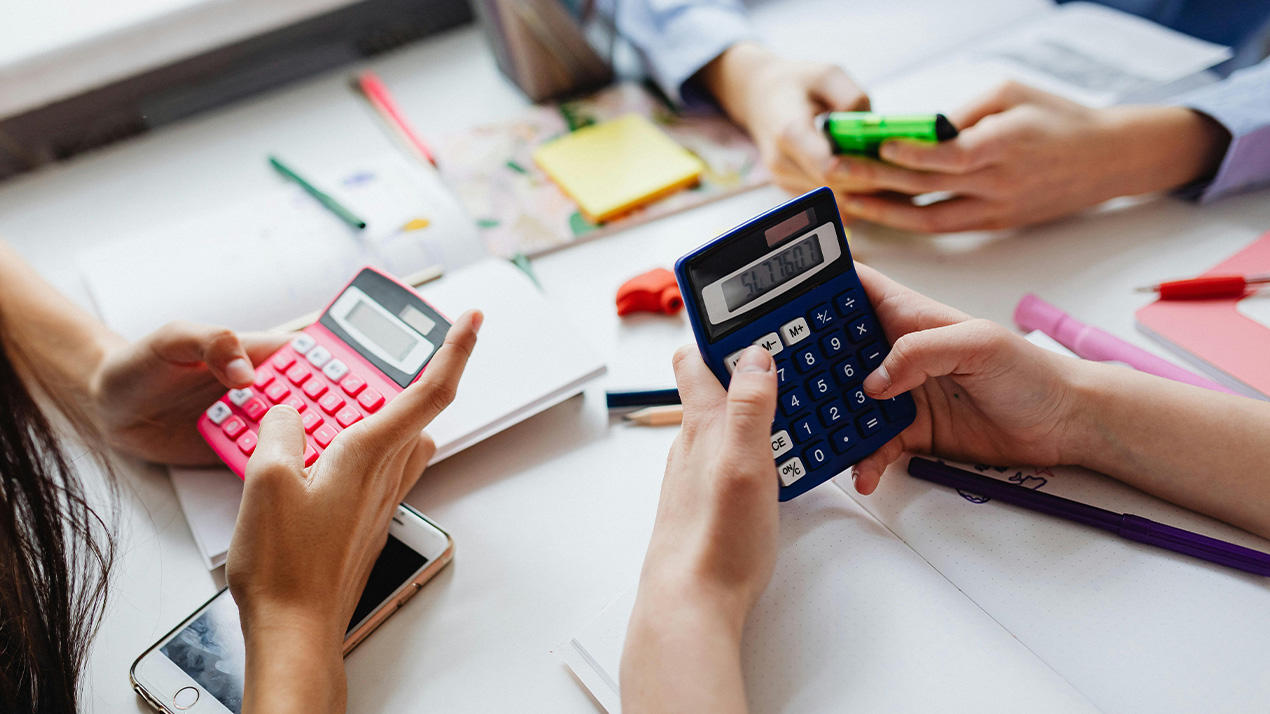 Three students sit around a table using calculators.