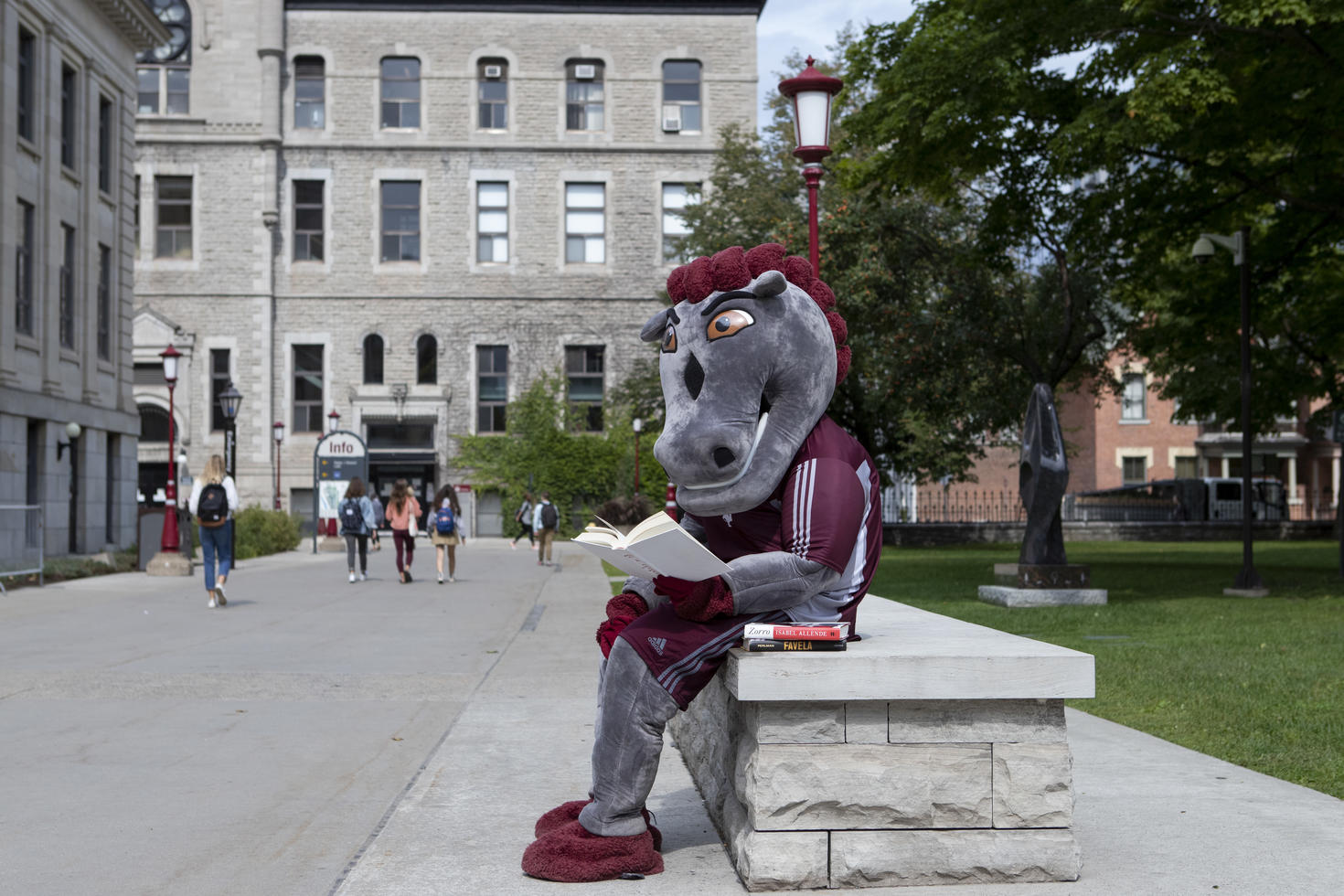 La mascotte des Gee-gees lisant un livre à l'extérieur d'un bâtiment sur le campus.